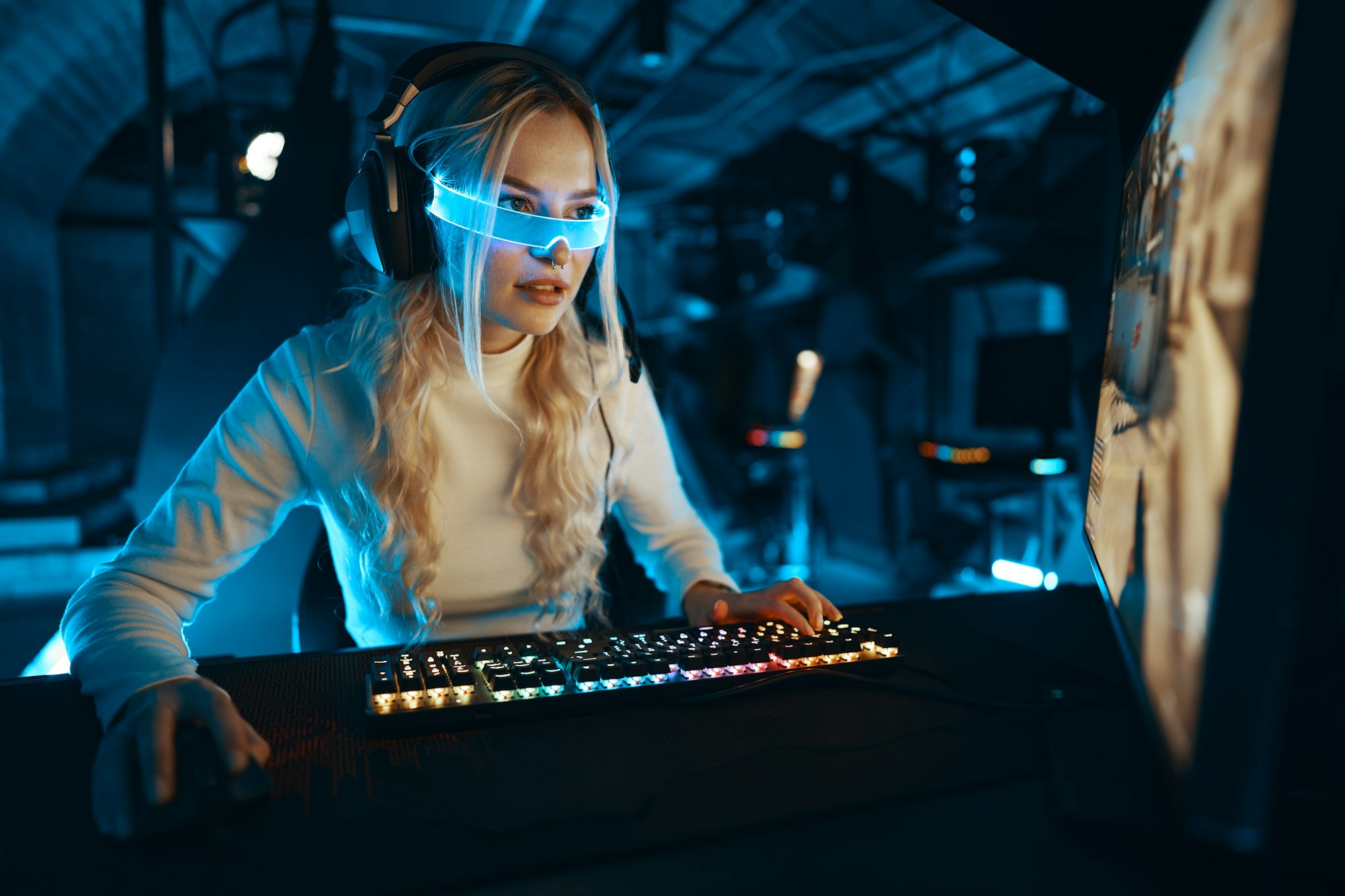 The blonde is playing a computer game. Blogger in neon futuristic glasses.