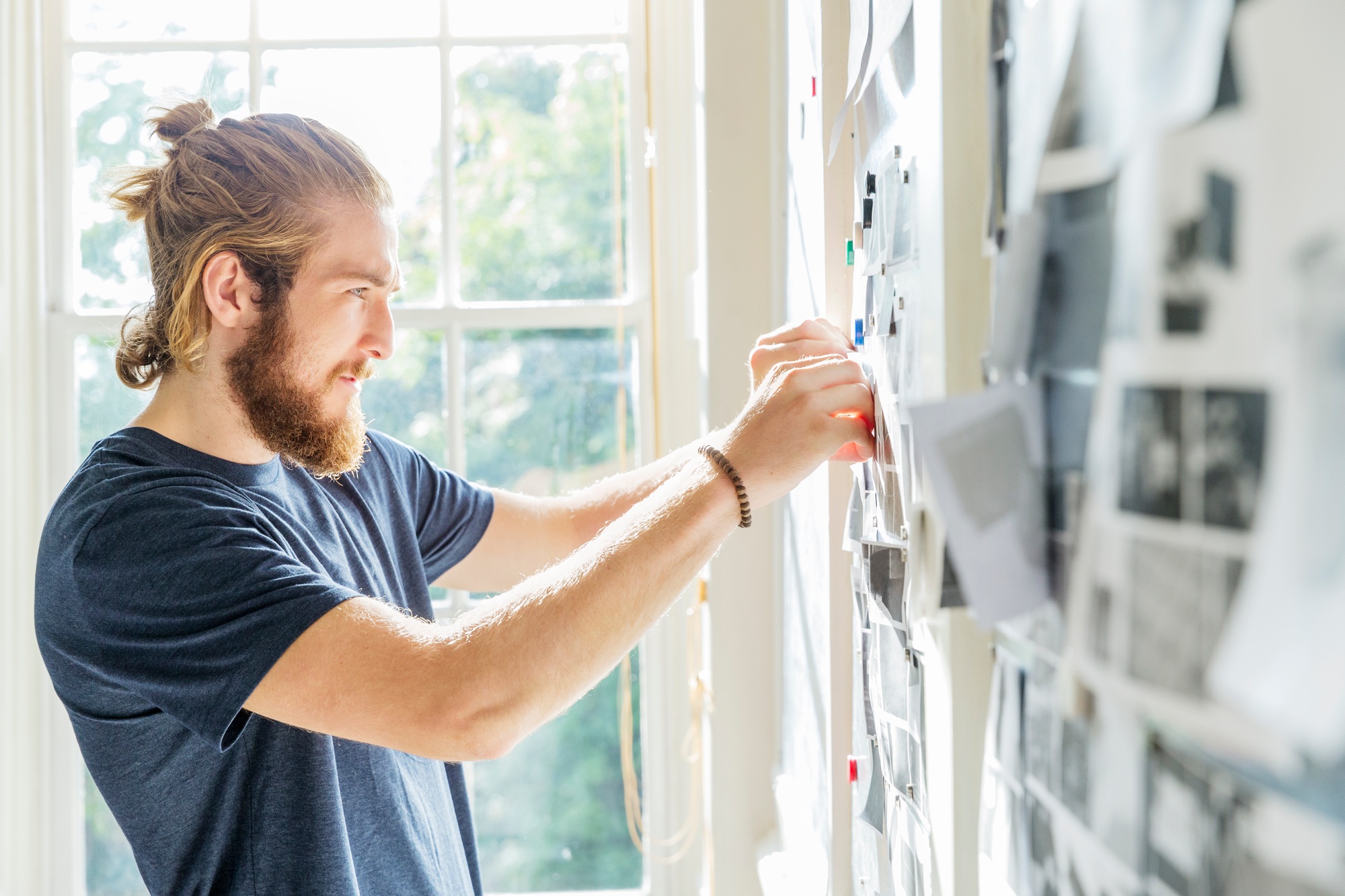 Young male designer pinning mood board ideas to wall in creative studio
